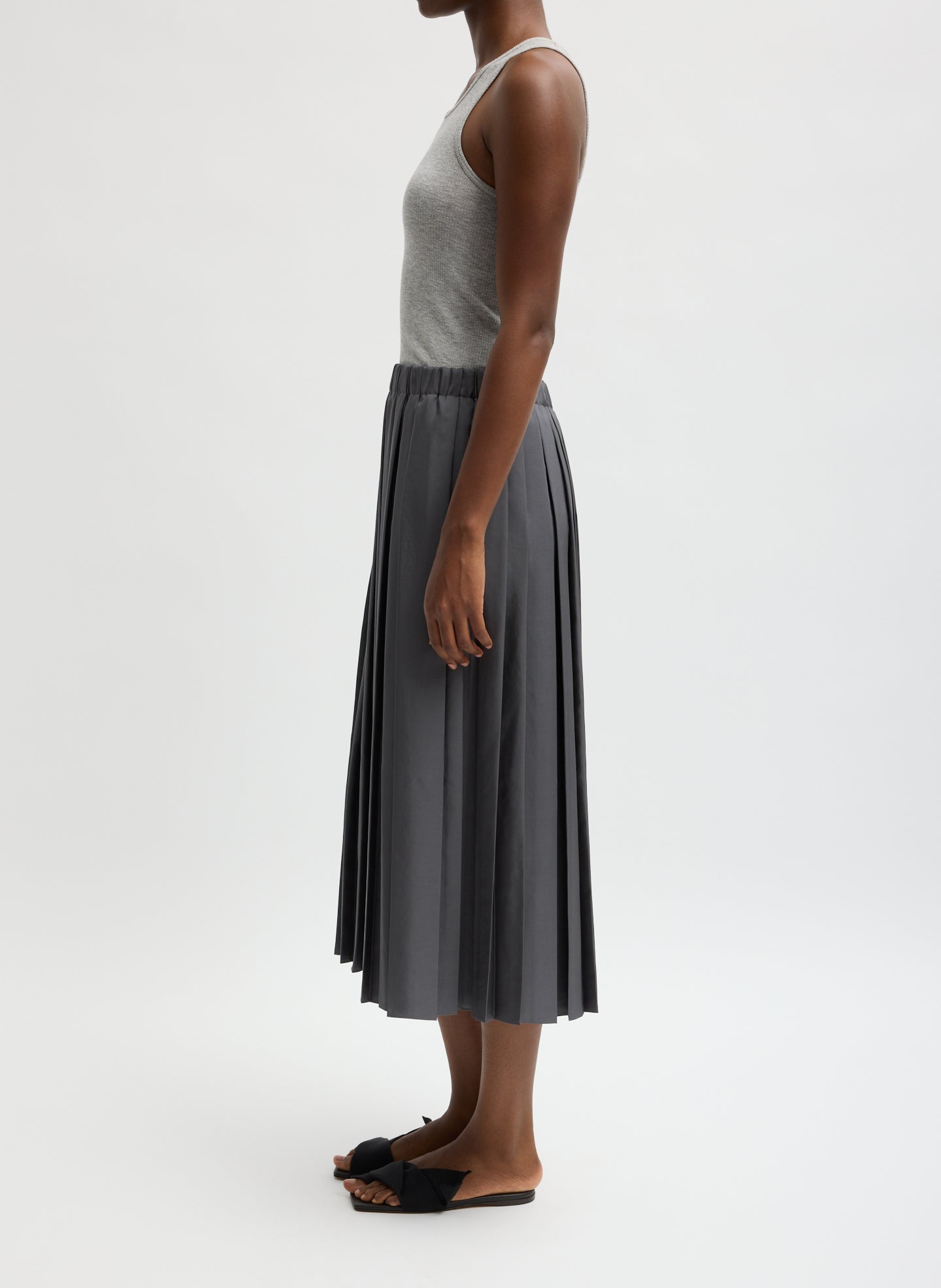 Woman wearing a gray pleated skirt and tank top on a white background facing the side