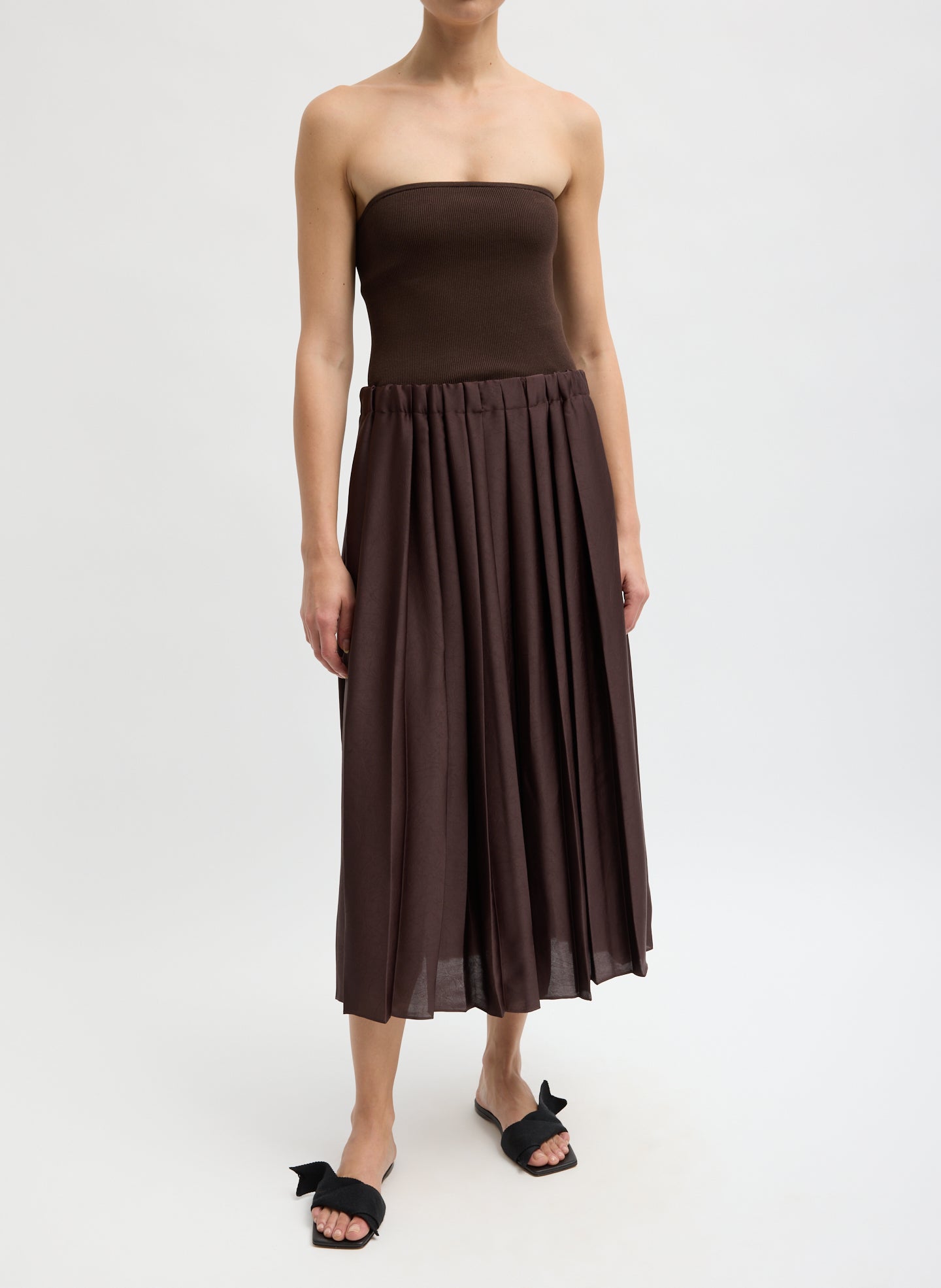 Woman wearing a brown strapless top and pleated skirt on a white background