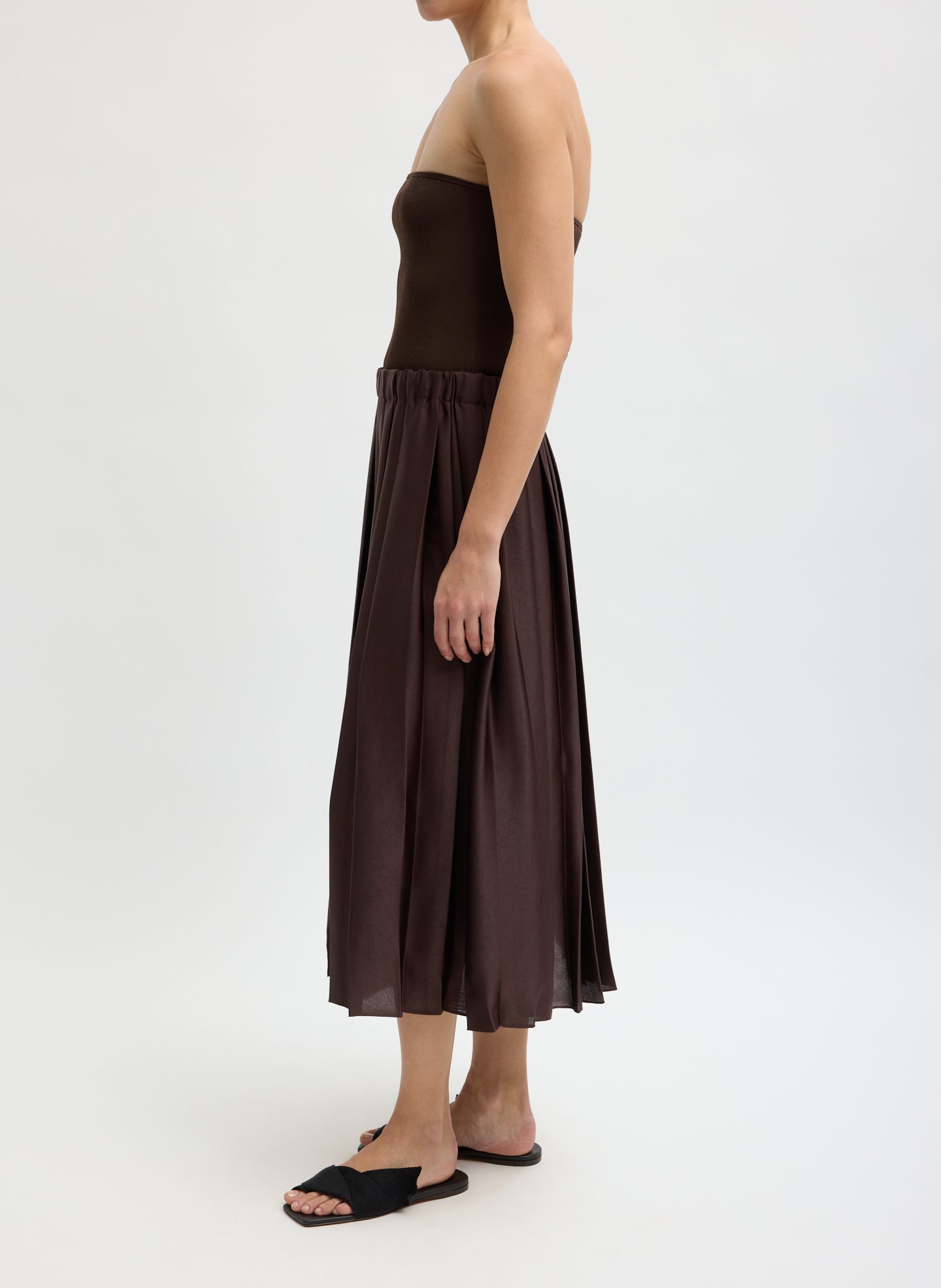 Woman wearing a brown strapless top and skirt on a white background turned to the side.
