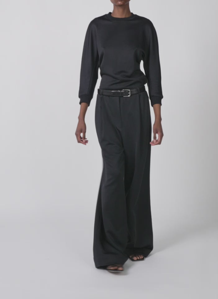 Model wearing the silk terry pleated pull on pant black walking forward and turning around