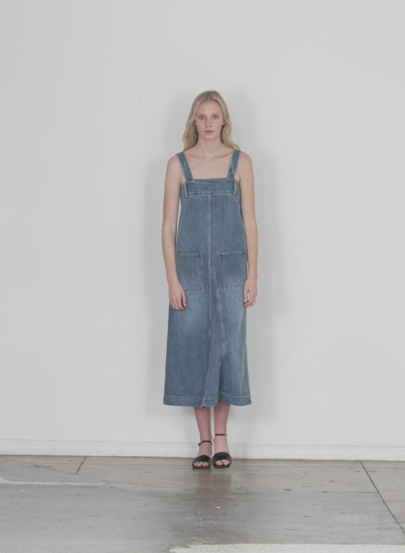 Model wearing the classic wash denim midi overall dress classic blue walking forward and turning around
