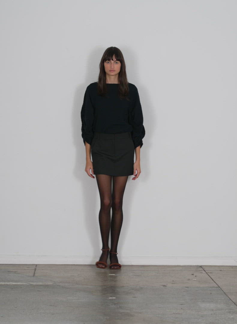 Model wearing the moue jersey boatneck ruched pleat sleeve top black navy multi walking forward and turning around
