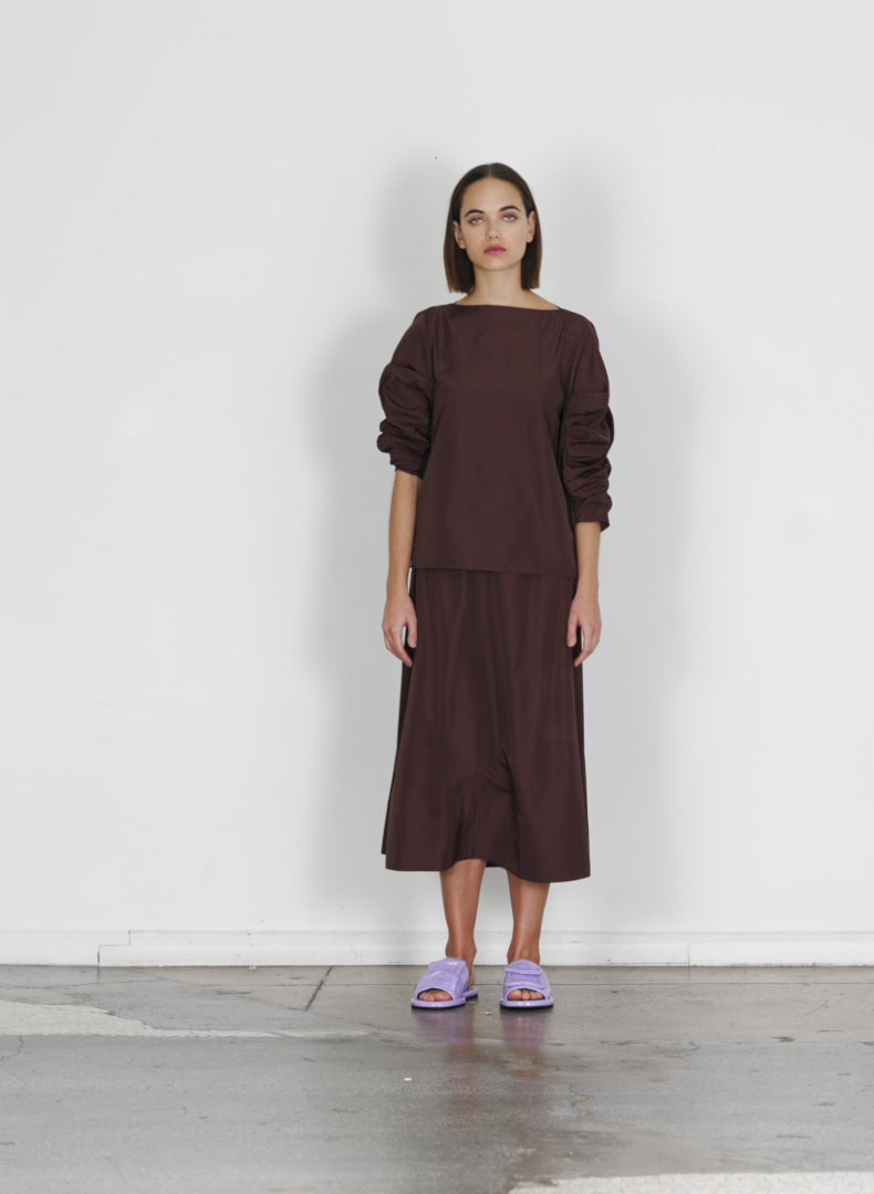 Model wearing the italian sporty nylon side shirred circle skirt dark brown walking forward and turning around