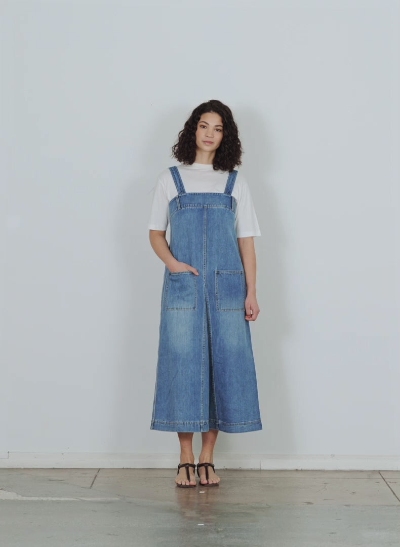 Model wearing the classic wash denim midi overall dress classic blue walking forward and turning around