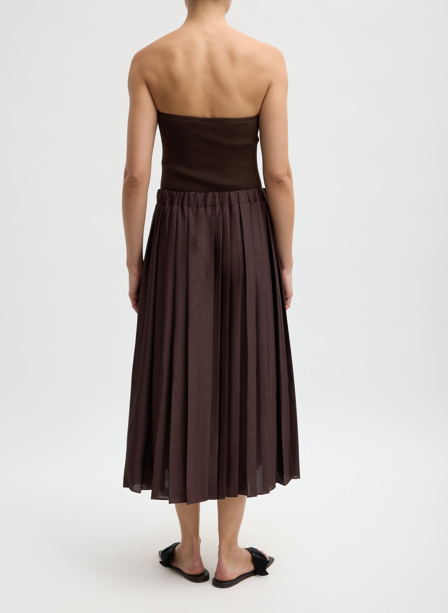 Brown strapless top and pleated skirt worn by a person on a white background from the back