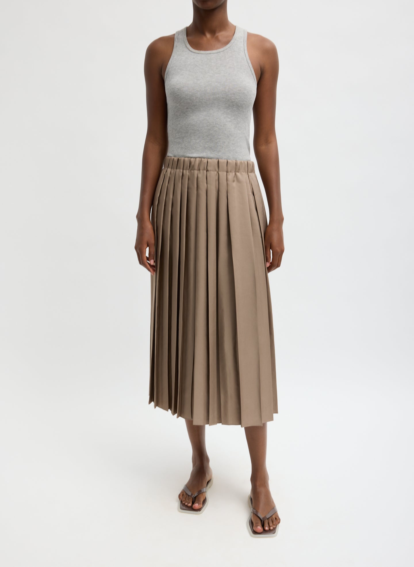 Woman wearing a gray tank top and beige pleated skirt on a white background