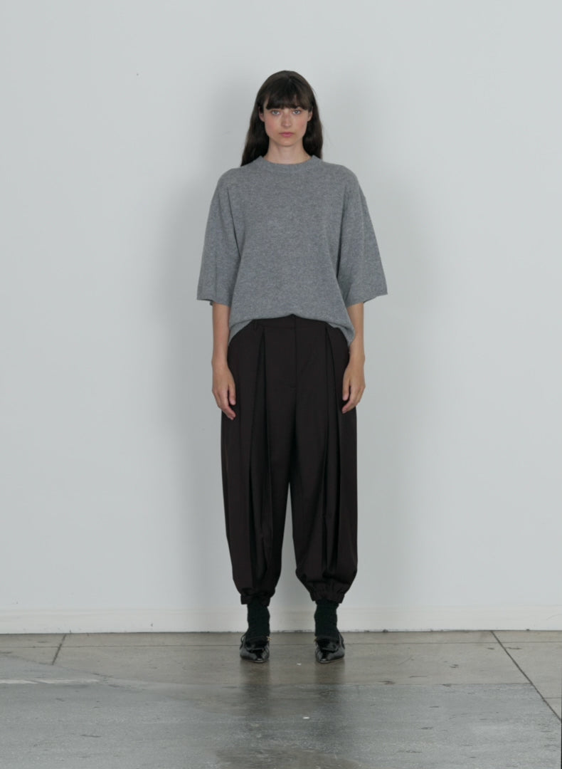 Model wearing the tropical wool pleated long balloon pant dark brown walking forward and turning around