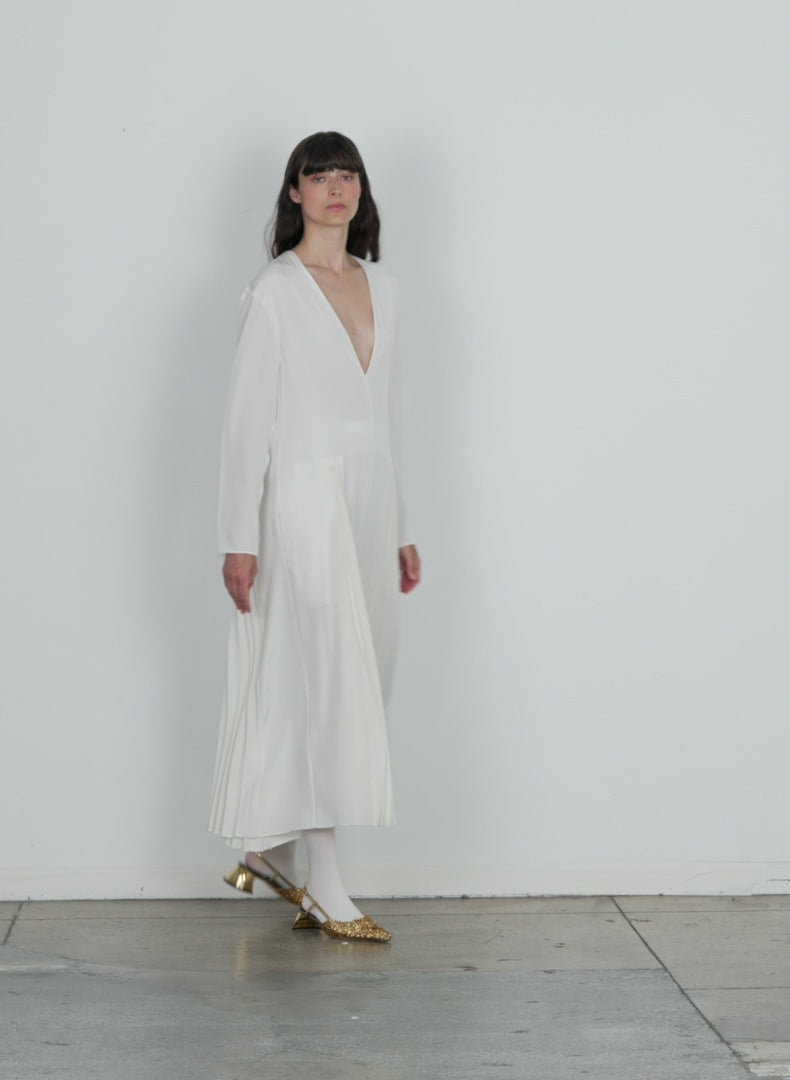 Model wearing the eco silk pleated godet dress white walking forward and turning around