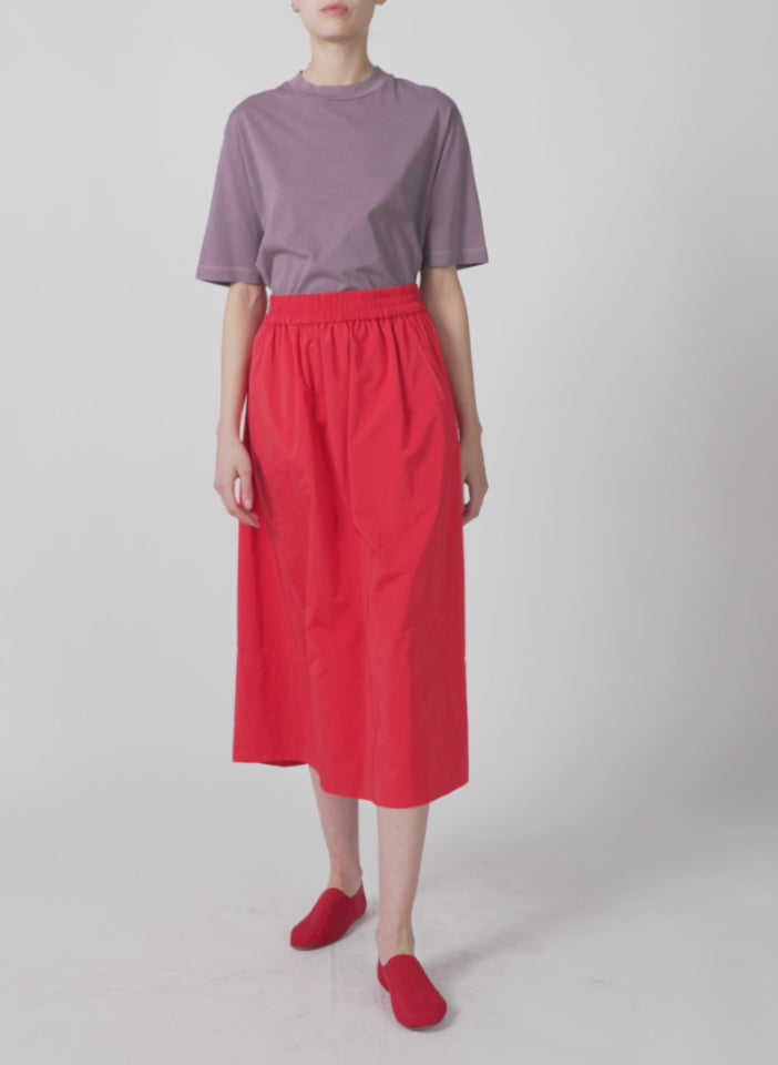 Model wearing the nylon pull on full skirt red walking forward and turning around