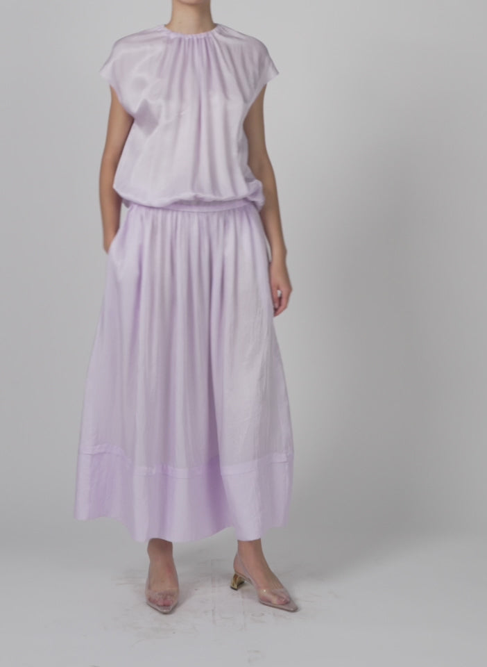 Model wearing the spring acetate shirred circular dress pale lavender walking forward and turning around
