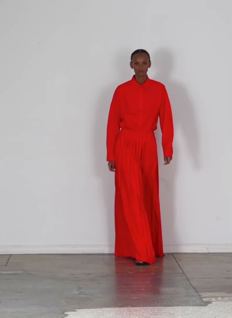 Model wearing the italian sporty nylon pleated pullon maxi skirt red walking forward and turning around