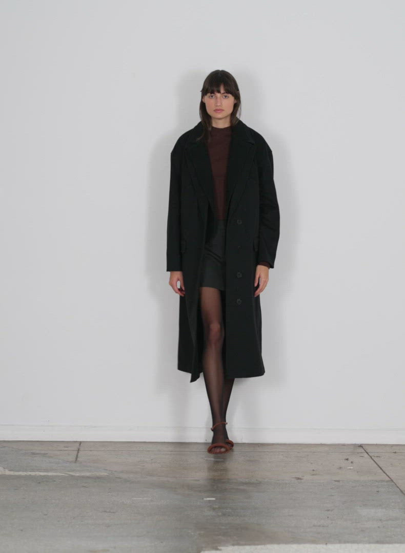 Model wearing the recycled wool cashmere liam western seamed coat black walking forward and turning around