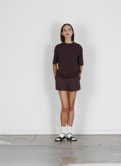 Model wearing the tshirt program mock neck unisex t dark brown 1 walking forward and turning around