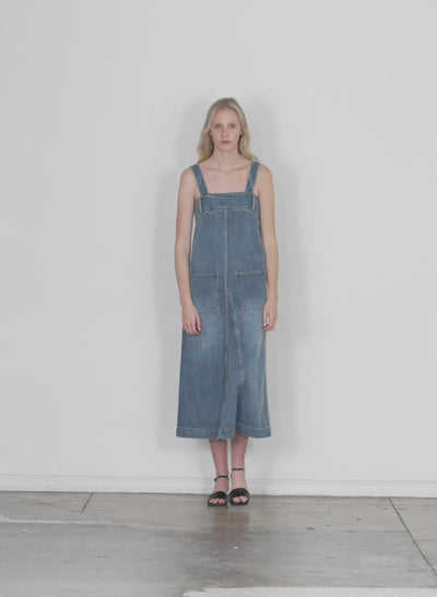 Model wearing the classic wash denim midi overall dress classic blue walking forward and turning around