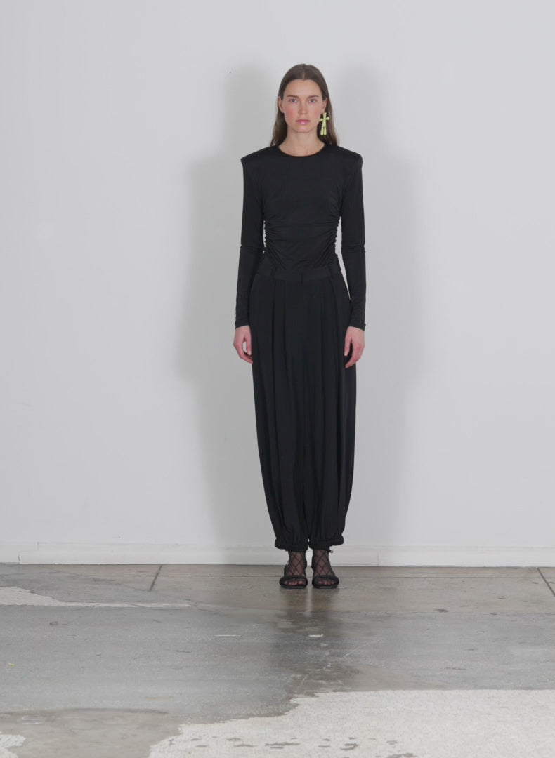 Model wearing the eco silk eden pleated balloon pant black walking forward and turning around