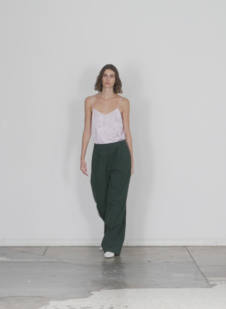 Model wearing the arun suiting asymmetrical pleat stella pant hazel green walking forward and turning around