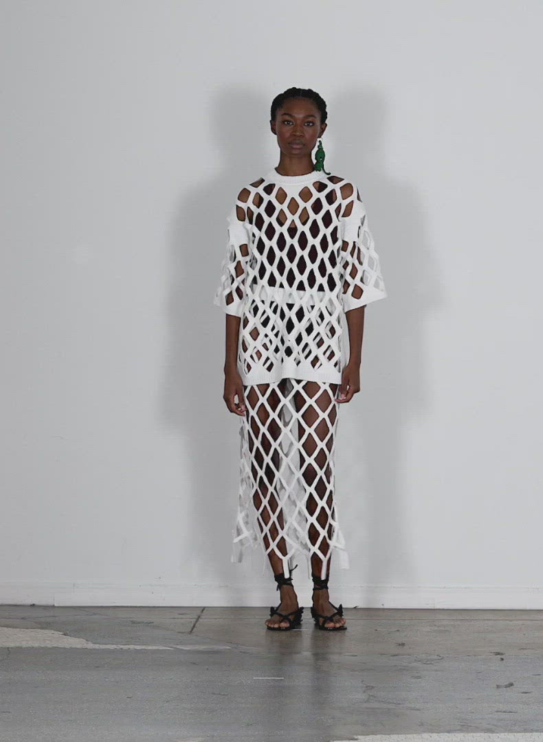 Model wearing the fishnet macrame sweater pullon skirt white walking forward and turning around