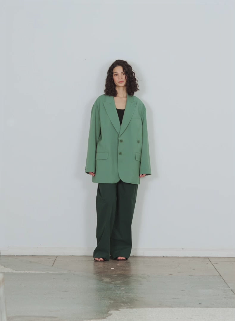 Model wearing the arun suiting asymmetrical pleat stella pant hazel green walking forward and turning around