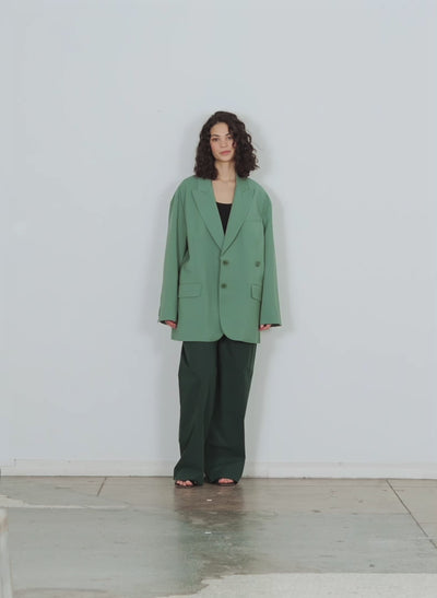 Model wearing the arun suiting asymmetrical pleat stella pant hazel green walking forward and turning around