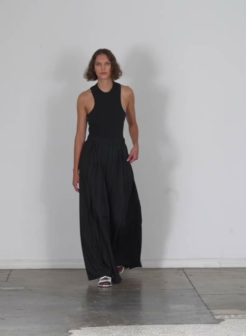 Model wearing the italian sporty nylon pleated pullon maxi skirt black walking forward and turning around