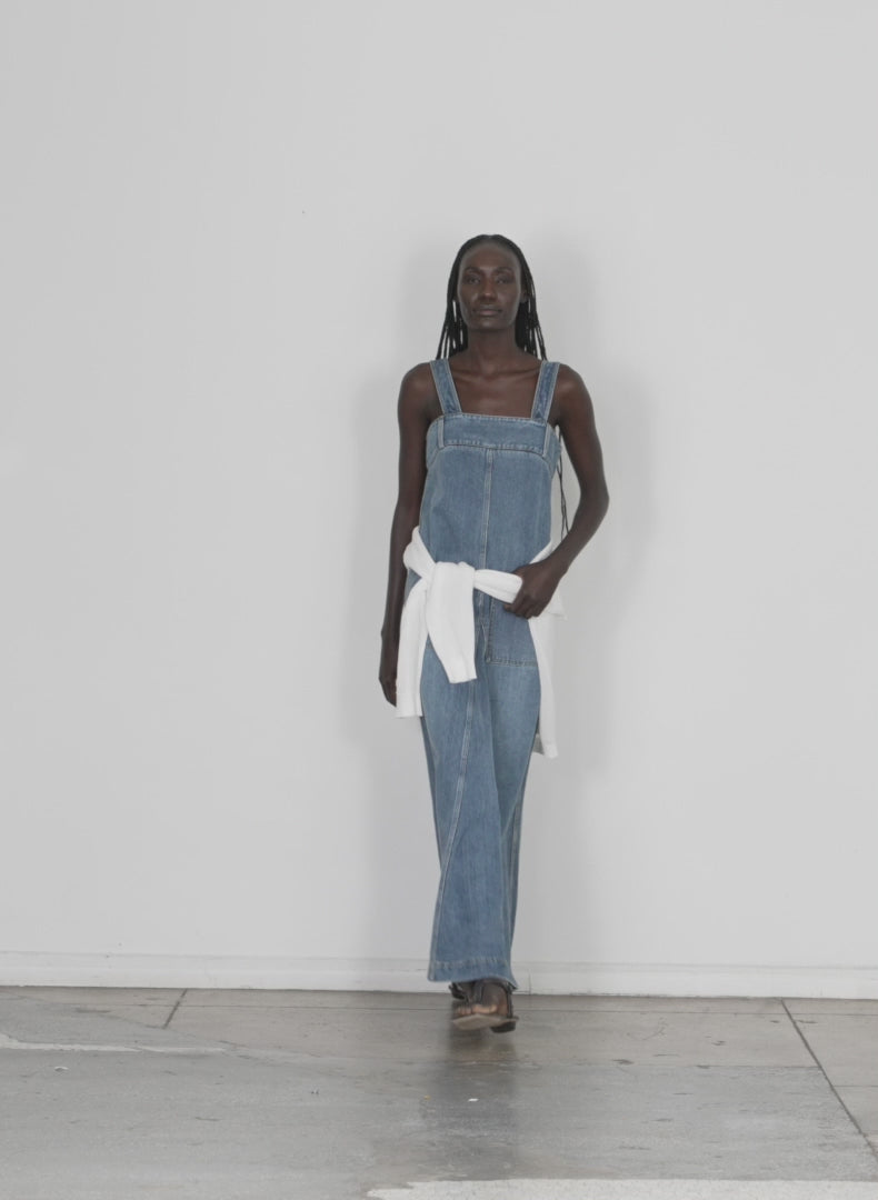 Model wearing the classic wash denim overall dress classic blue walking forward and turning around