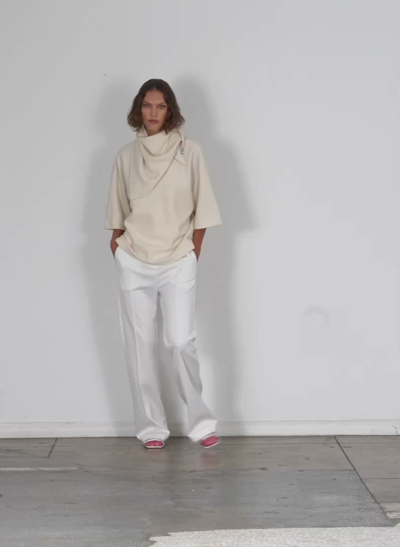 Model wearing the boiled wool sculpted funnel neck top ivory walking forward and turning around