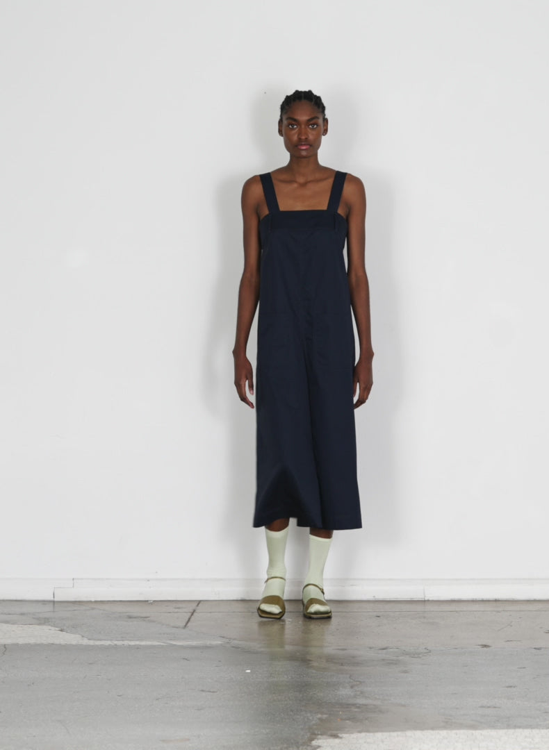 Model wearing the eco poplin overall midi dress dark navy walking forward and turning around